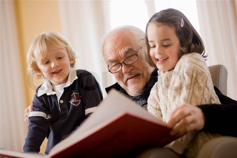 Old man reading book to children, stock photo