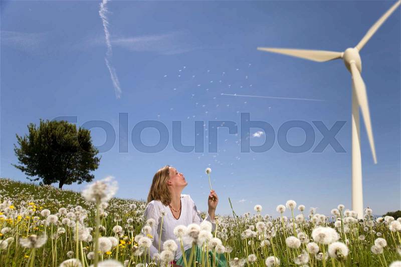 Woman blowing dandelion at wind turbine, stock photo