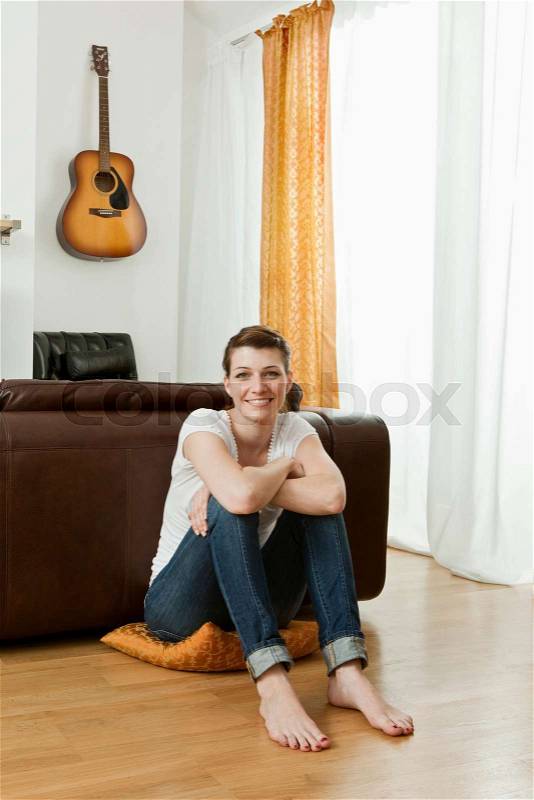 Young woman sitting on living room floor, stock photo
