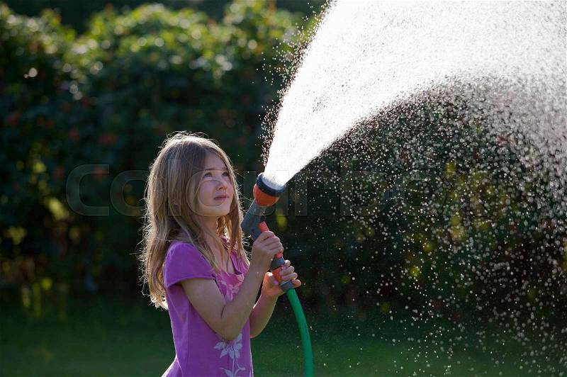 Young girl spraying water with a hose, stock photo