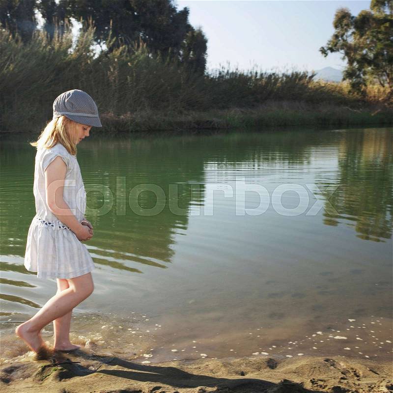 Young girl by river with feet in water, stock photo