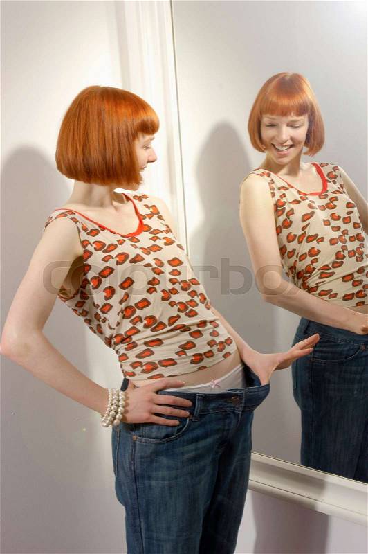 Woman looking at weight loss in mirror, stock photo
