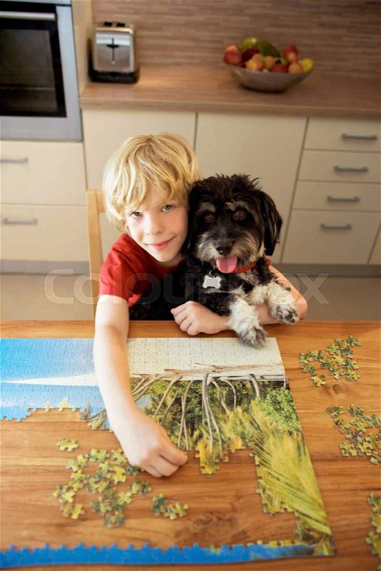 A boy holding a dog while doing a puzzle, stock photo