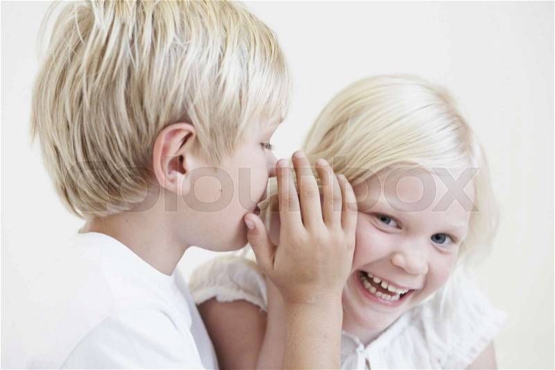 Young boy whispering into girl\'s ear, stock photo