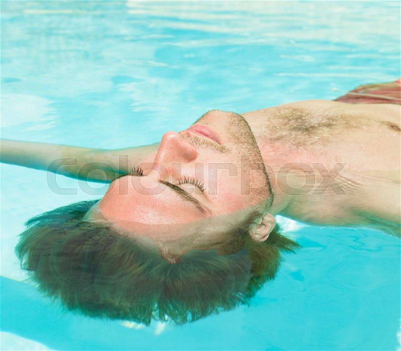 Young man floating in water, stock photo