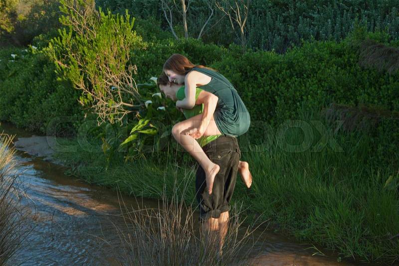 Man carrying girl on back through stream, stock photo