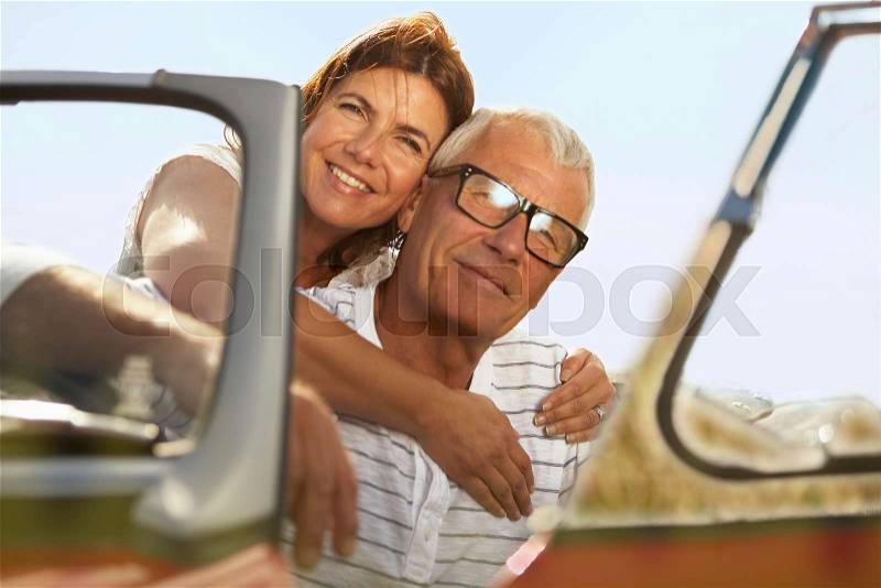 Senior couple embracing in sports car, stock photo