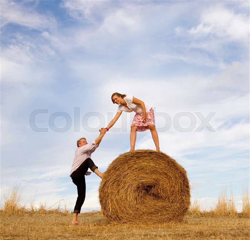 Woman helping man to climb hay bale, stock photo