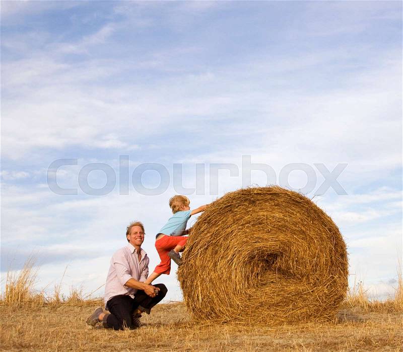 Man helping boy to climb hay bale, stock photo