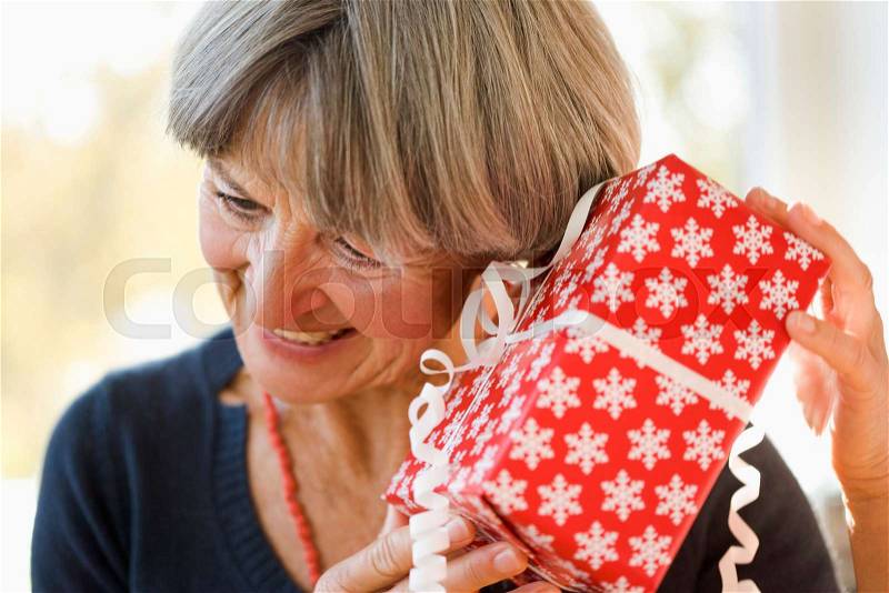 Old woman holding ear against present, stock photo
