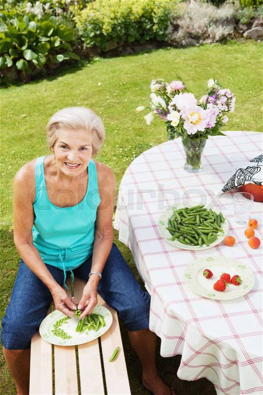 Mature woman peeling pods in garden, stock photo