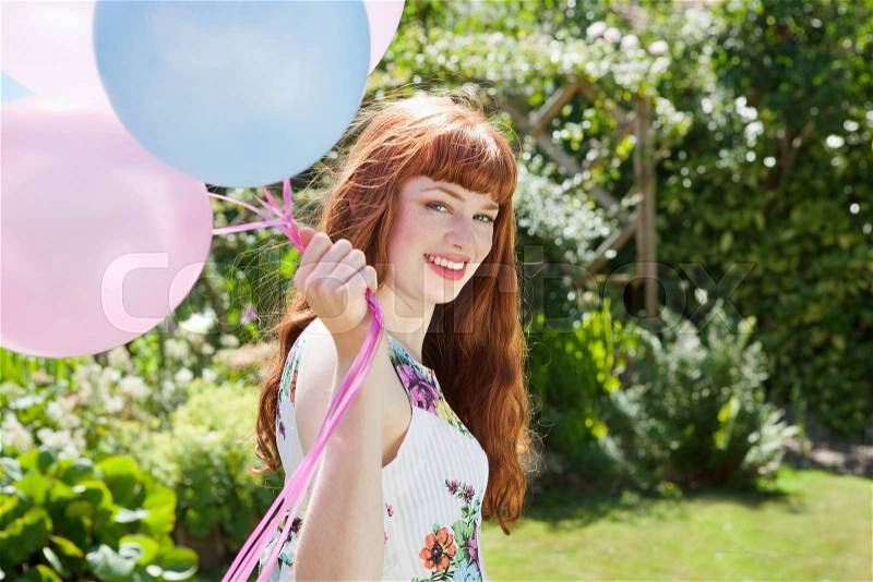 Young woman holding balloons in garden, stock photo