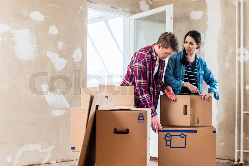 Young couple in love opening cardboard boxes during the renovation of their new home after moving in together, stock photo