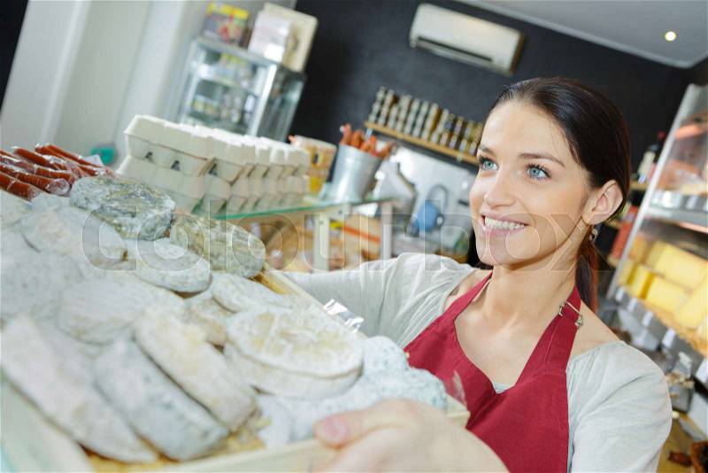 Saleswoman selling cheese to man in grocery store, stock photo