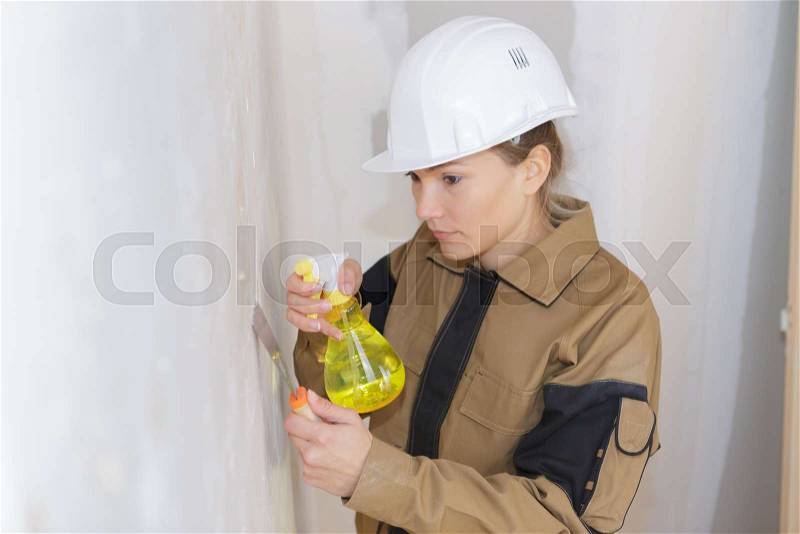 Builder woman wiping white wall with wet cloth, stock photo
