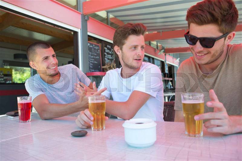 Three male friends relax drinking beer at restaurant terrace, stock photo