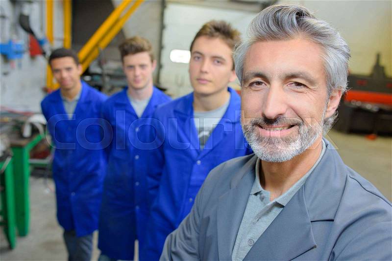 Smiling teacher with students stood behind him, stock photo