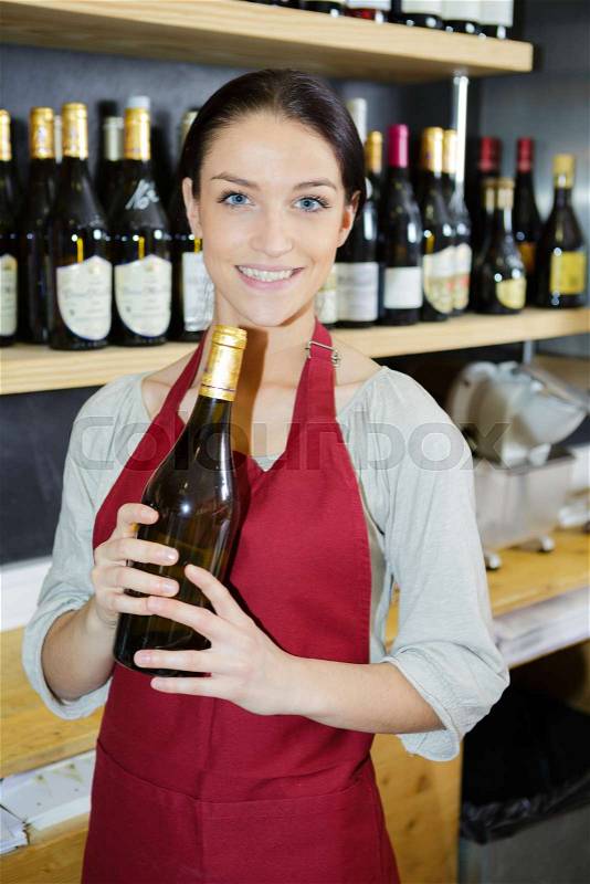 Smiling female sommelier presenting a wine bottle, stock photo