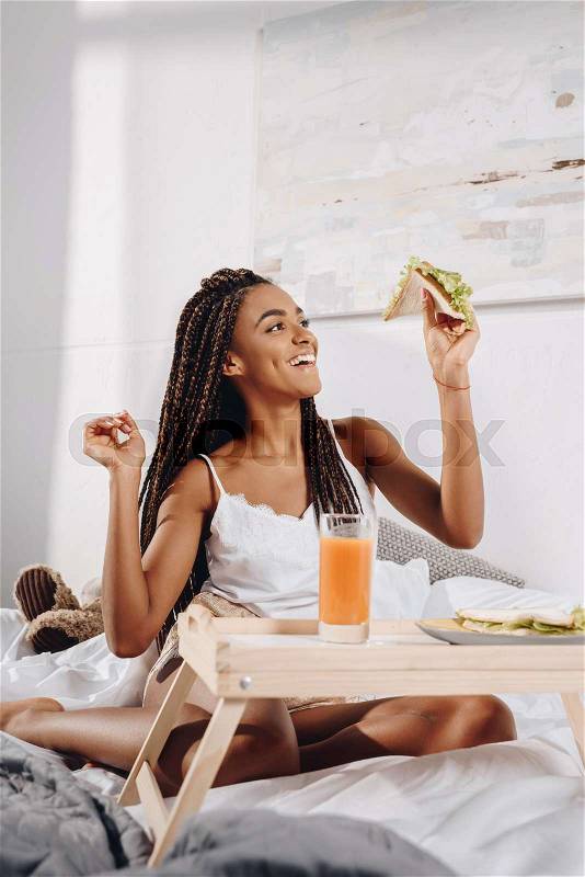 Happy african american woman eating breakfast in bed, stock photo