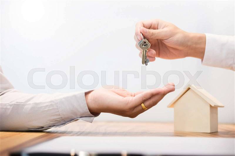 Estate agent in suit sitting in an office desk Handing over of house keys with customer after contract signature, stock photo