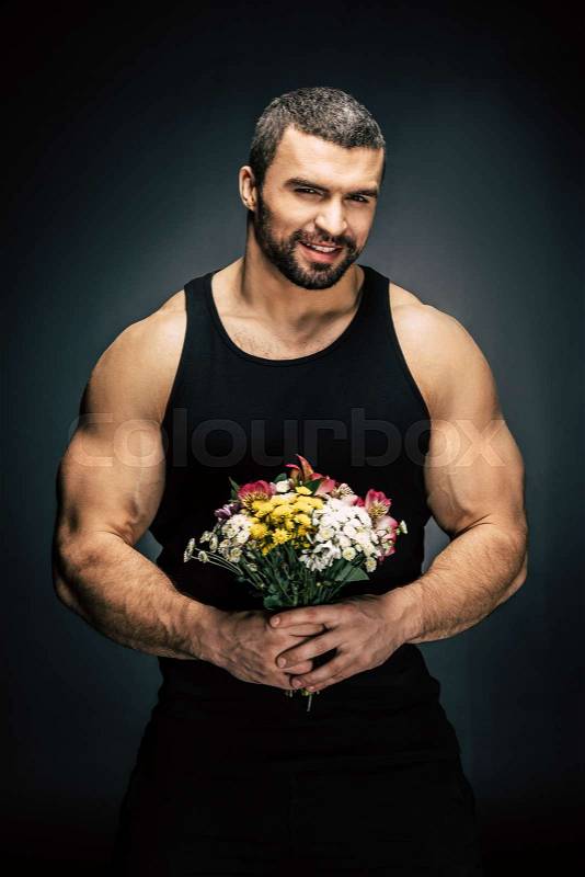 Portrait of smiling sportive man with bouquet of flowers in hands isolated on black, stock photo