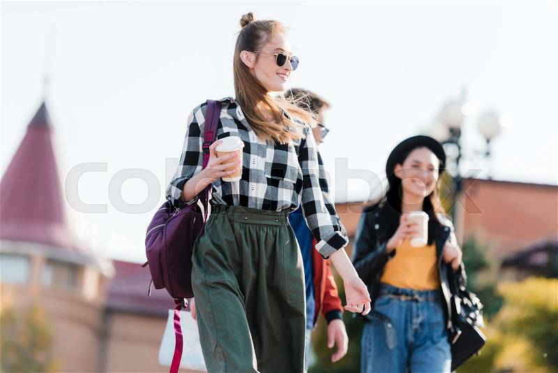 Multicultural friends with coffee to go in hands walking on street, stock photo