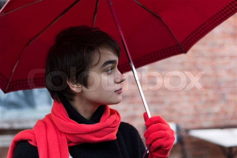 Portrait of young melancholy woman in a red scarf under unmbrella on the rainy street. Concept of loneliness. Copy space, stock photo