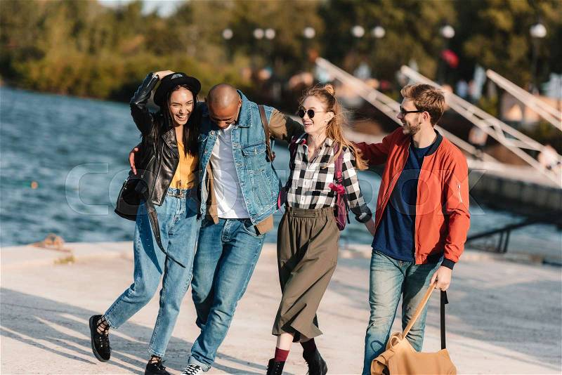 Group of cheerful multicultural friends walking on pier together, stock photo