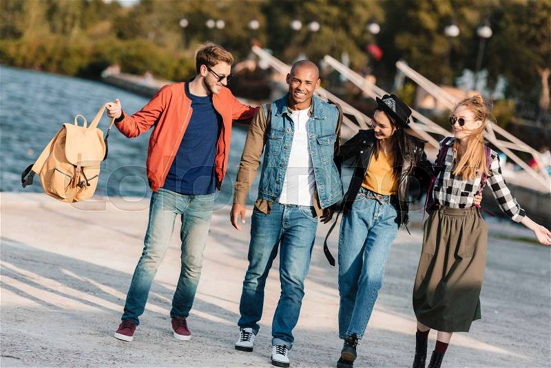 Group of cheerful multicultural friends walking on pier together, stock photo