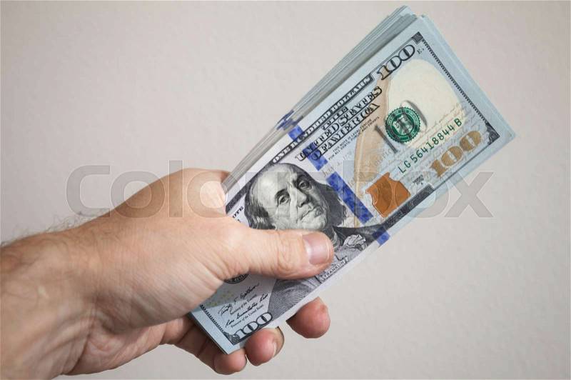 Bundle of One Hundred Dollars notes in male hand over gray wall background, stock photo