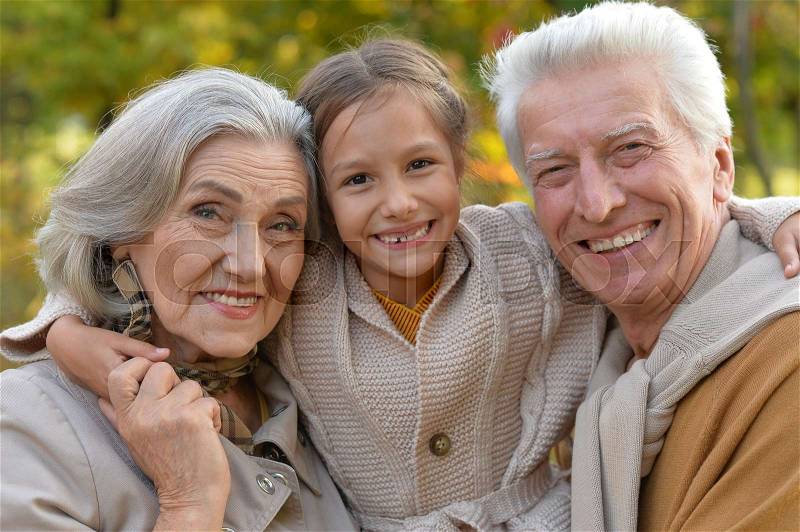 Portrait of smiling grandparents and granddaughter in park, stock photo