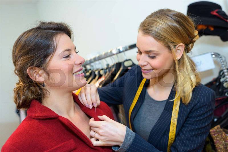 Cheerful smiling woman trying on coat in womens cloth store, stock photo