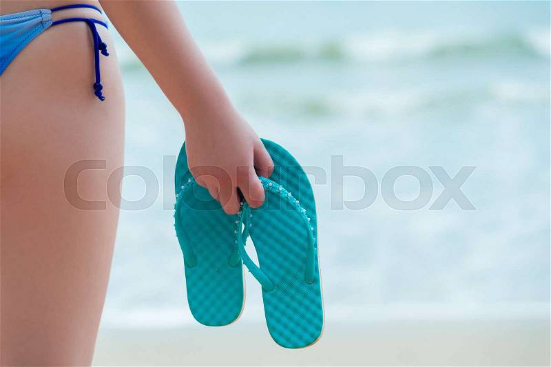 Flip flops in the hand of a girl on the beach closeup, stock photo