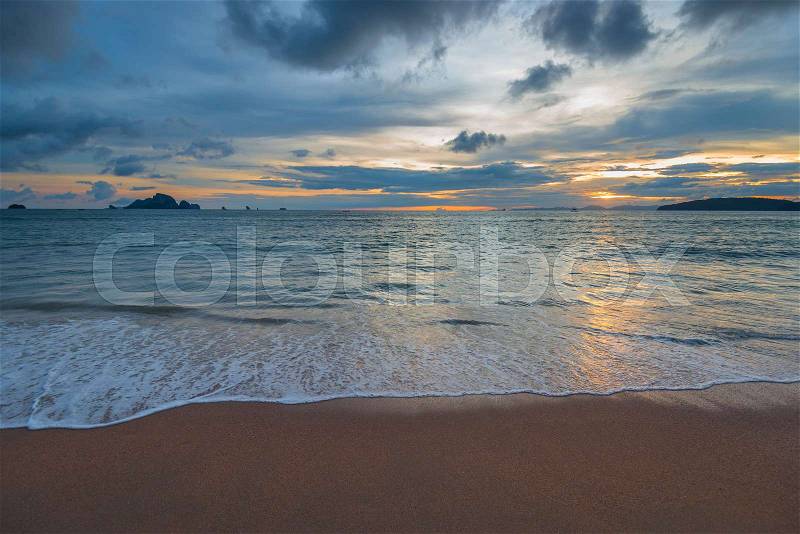 Beautiful waves and sandy shore, on the horizon the sun sets over the mountains, stock photo