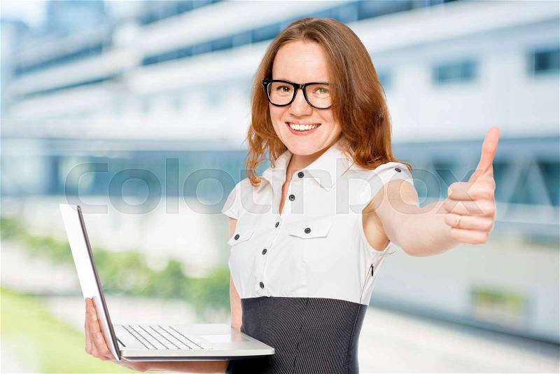 Successful woman with a laptop holding a thumb up in the office, stock photo