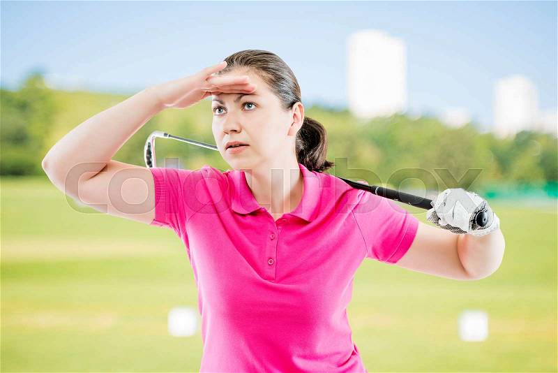 Woman in pink T-shirt with a golf club looks into the distance on a background of golf courses, stock photo