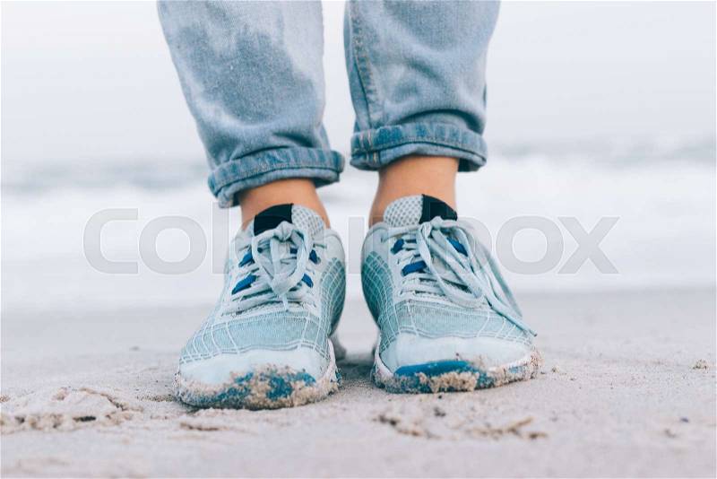 Female feet in wet jeans and sneakers on the beach close-up, stock photo