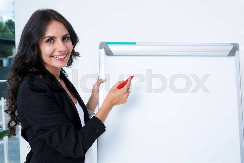 Smiling pregnant businesswoman writing on whiteboard with red marker pen, stock photo