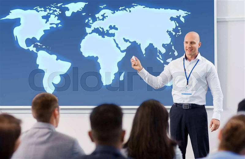 Business, education and people concept - smiling businessman or lecturer with world map on projection screen and group of students at conference presentation or lecture, stock photo