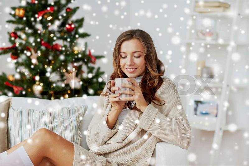Christmas, holidays and people concept - happy young woman with cup of coffee or tea at home over snow, stock photo