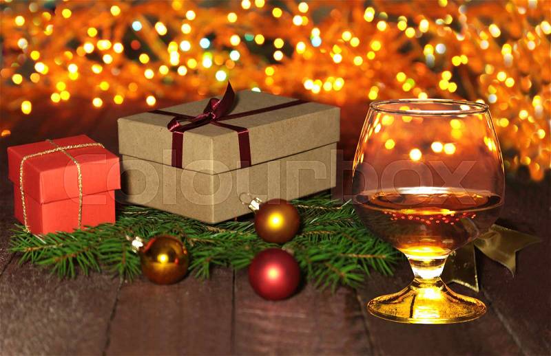 Glass with cognac or whiskey, gift box, colored balls and christmas tree on wooden table. Celebrities composition. Selective focus, stock photo