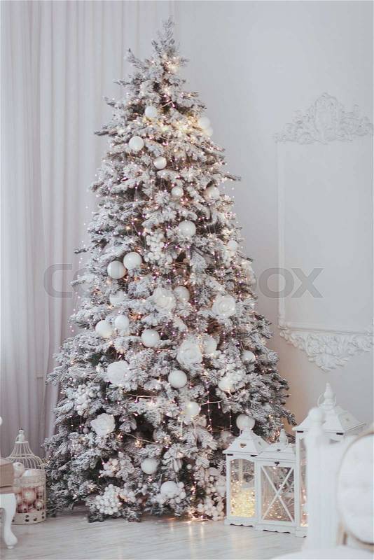 Holiday decorated room with Christmas tree covered with snow and toys. White interior with lights, stock photo