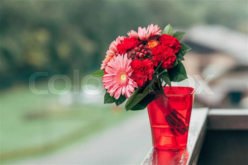 A bouquet of different red flowers in a red plastic vase on a table. Close-up. Artwork. Copy space. Outdoors, stock photo