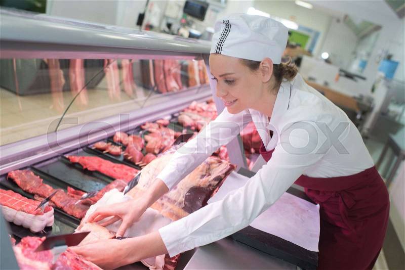 Happy female butcher in meat store counter, stock photo