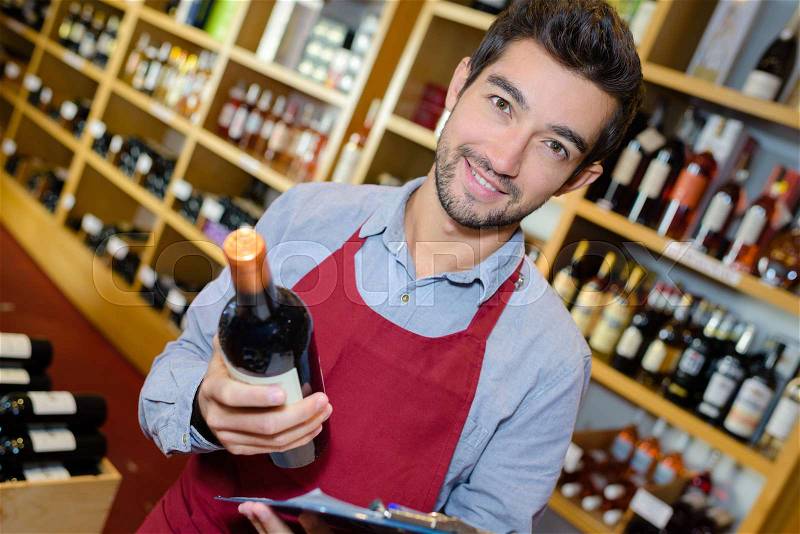Smiling man seller having bottle of wine in shop, stock photo