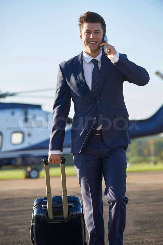 Businessman Walking Away From Helicopter Whilst Talking On Mobile Phone, stock photo