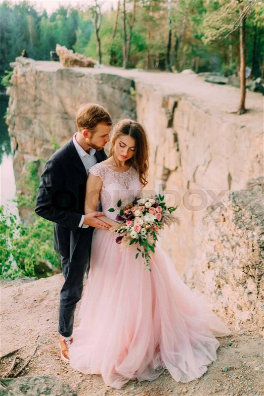 Happy newlyweds embracing. Man in tuxedo and woman in a pink wedding dress is posing on nature. A ceremony outdoors. Close-up portrait, stock photo