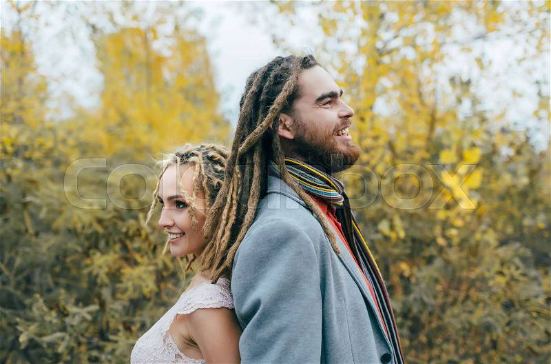 A cheerful couple stands back to back. Bride and groom with dreadlocks having fun on nature. Wedding ceremony outdoors. Close-up portrait, stock photo