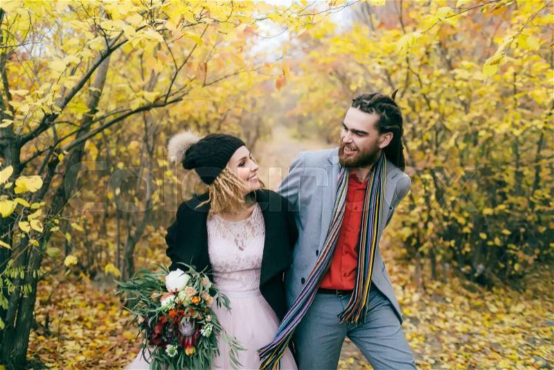 A happy couple is walking on a trail in an autumn forest. Bride and groom with dreadlocks are looking at each other on nature. Wedding ceremony outdoors.. Close-up portrait, stock photo