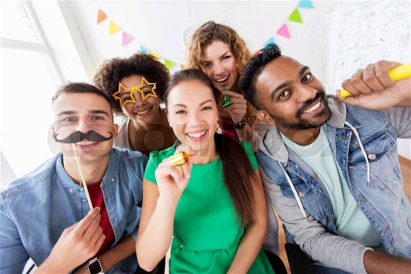 Corporate, celebration and holidays concept - happy friends or team with party accessories having fun at office, stock photo